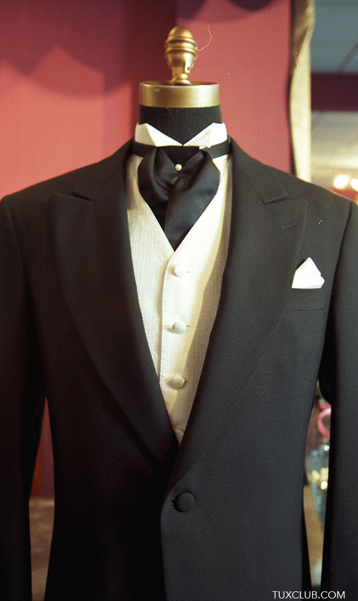 Black morning suit with white vest and black ascot on a mannequin against a red background.