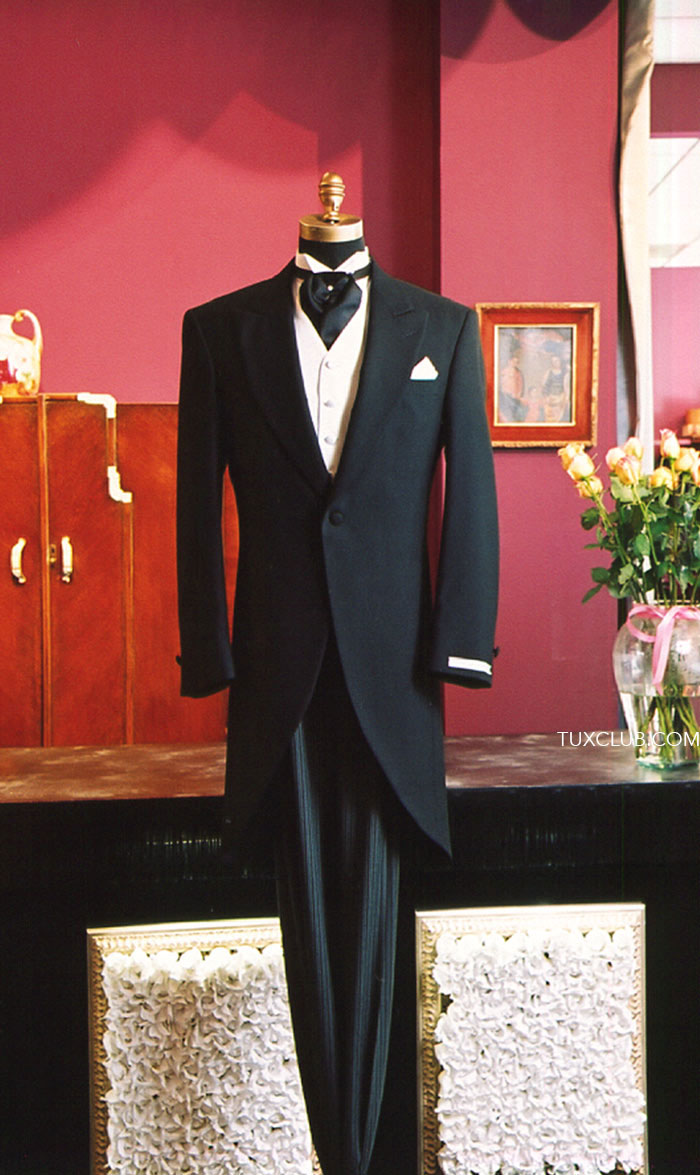 full length mannequin wearing a black cutaway morning suit against a red wall with a vase of flowers.