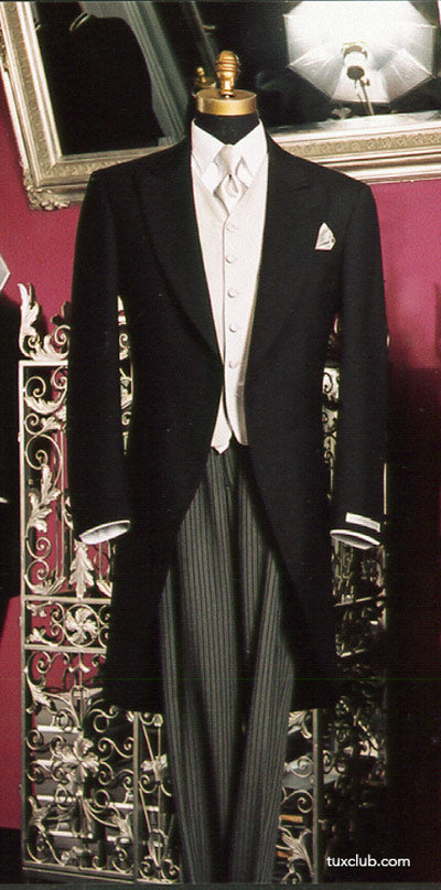 Black morning suit with silver long dress tie and vest and gray pants on a mannequin against a decorative wall.