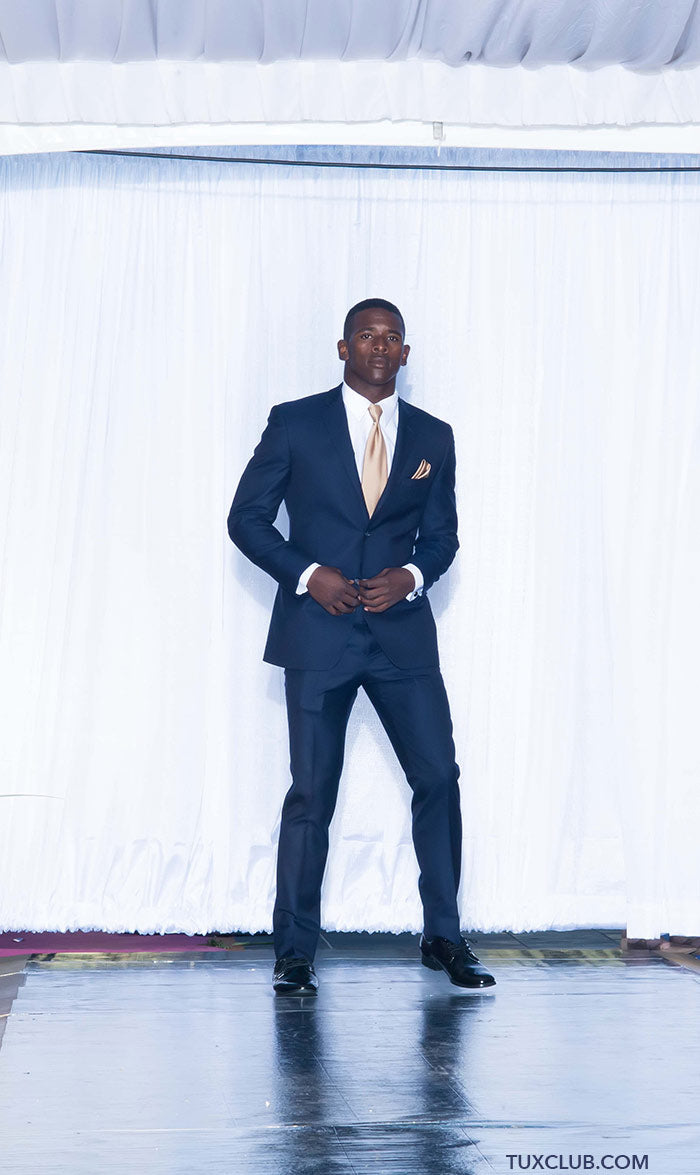 Handsome black man wearing a navy slim-fit suit with a white shirt and gold tie on a stage