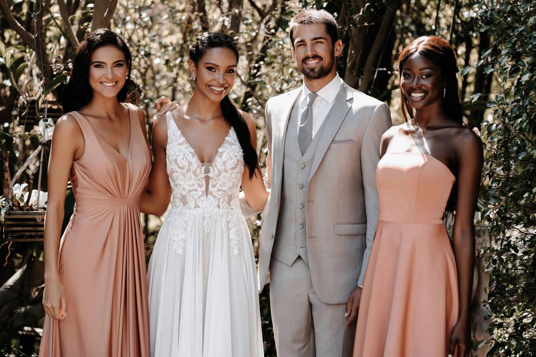 Groom wearing sand colored wedding suit by tuxclub accompanied by a bride and 2 bridemaids wearing coral dresses.