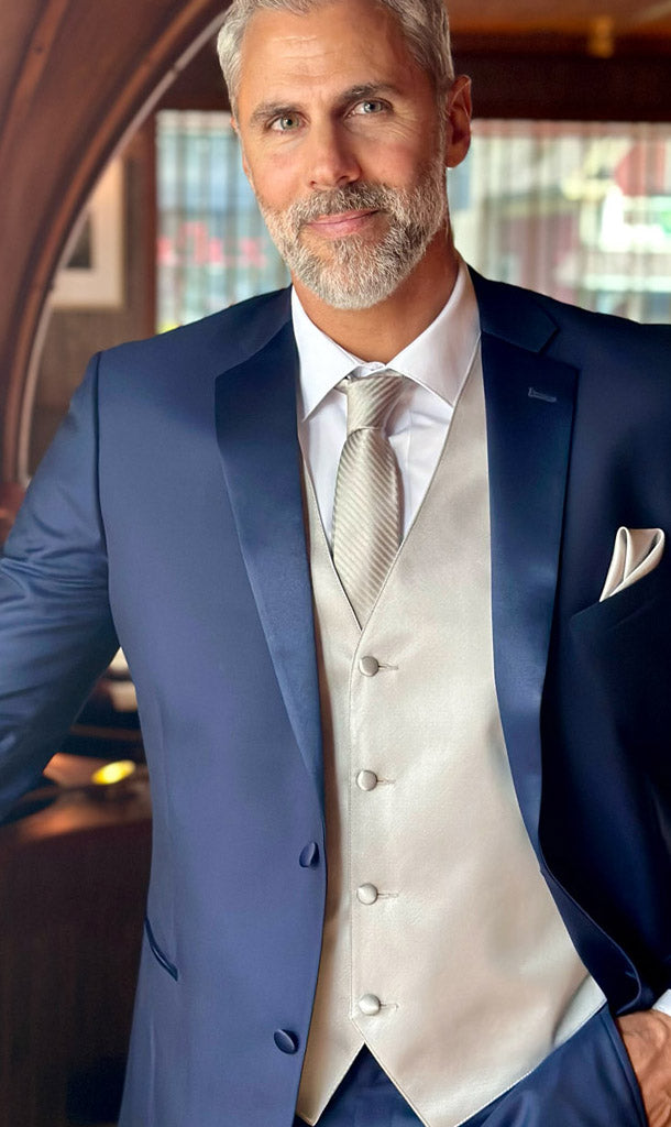 Close-up front view of a Man wearing a navy blue notch lapel tuxedo with a gray vest and gray long tie in a fancy restaurant.
