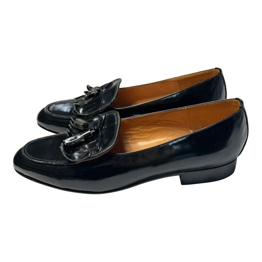 Pair of black patent leather loafers with tassels on a white background