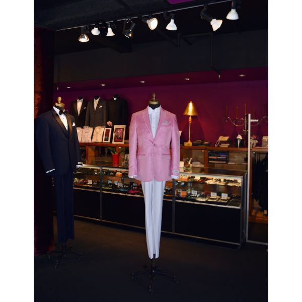 Full length mannequin wearing a pink dinner jacket with white pants and white bowtie on display inside a tuxedo shop
