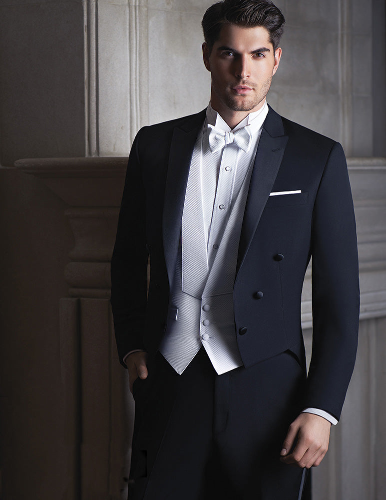 man wearing black tailcoat tuxedo with white shirt and white pique vest and bowtie against a neutral background