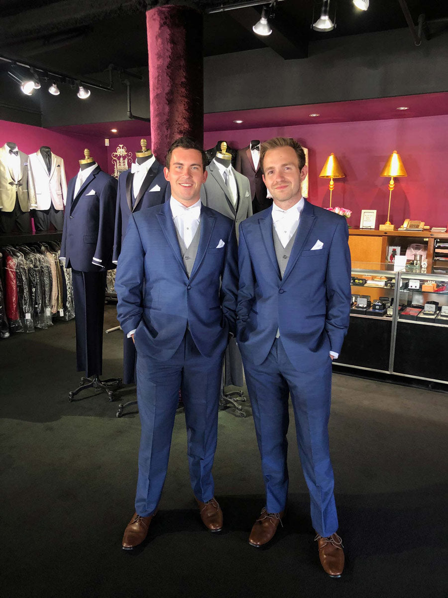 Two men in new-blue peak lapel tuxedos standing in a tuxedo shop