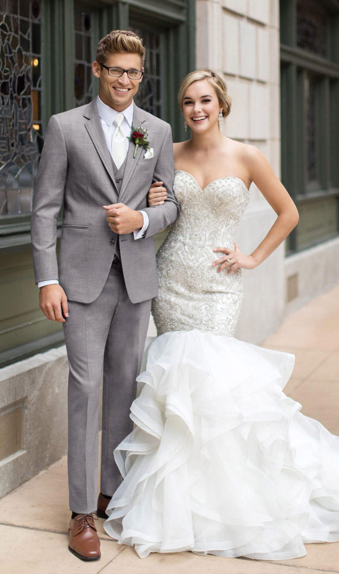 groom and bride with groom wearing 3 piece slim fit gray suit and white dress tie and the bride in white gown on sidewalk