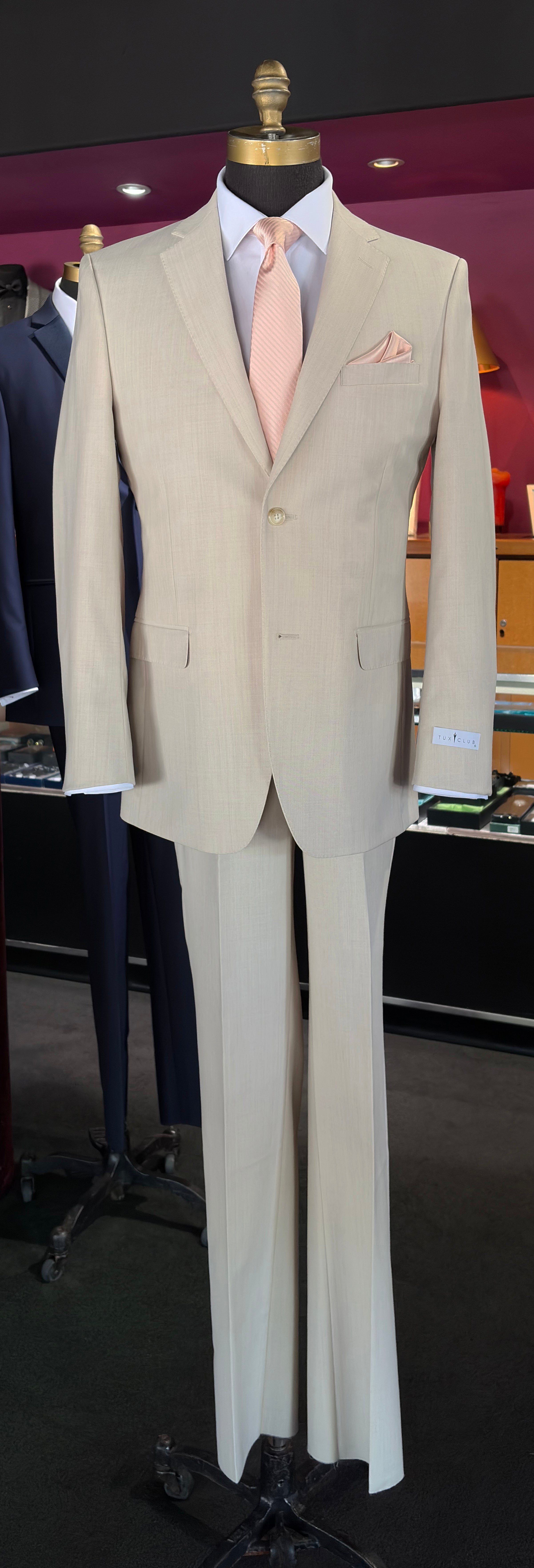 Life size mannequin wearing a tan fitted suit with a petal color necktie and a petal pocket handkerchief inside a tuxedo shop