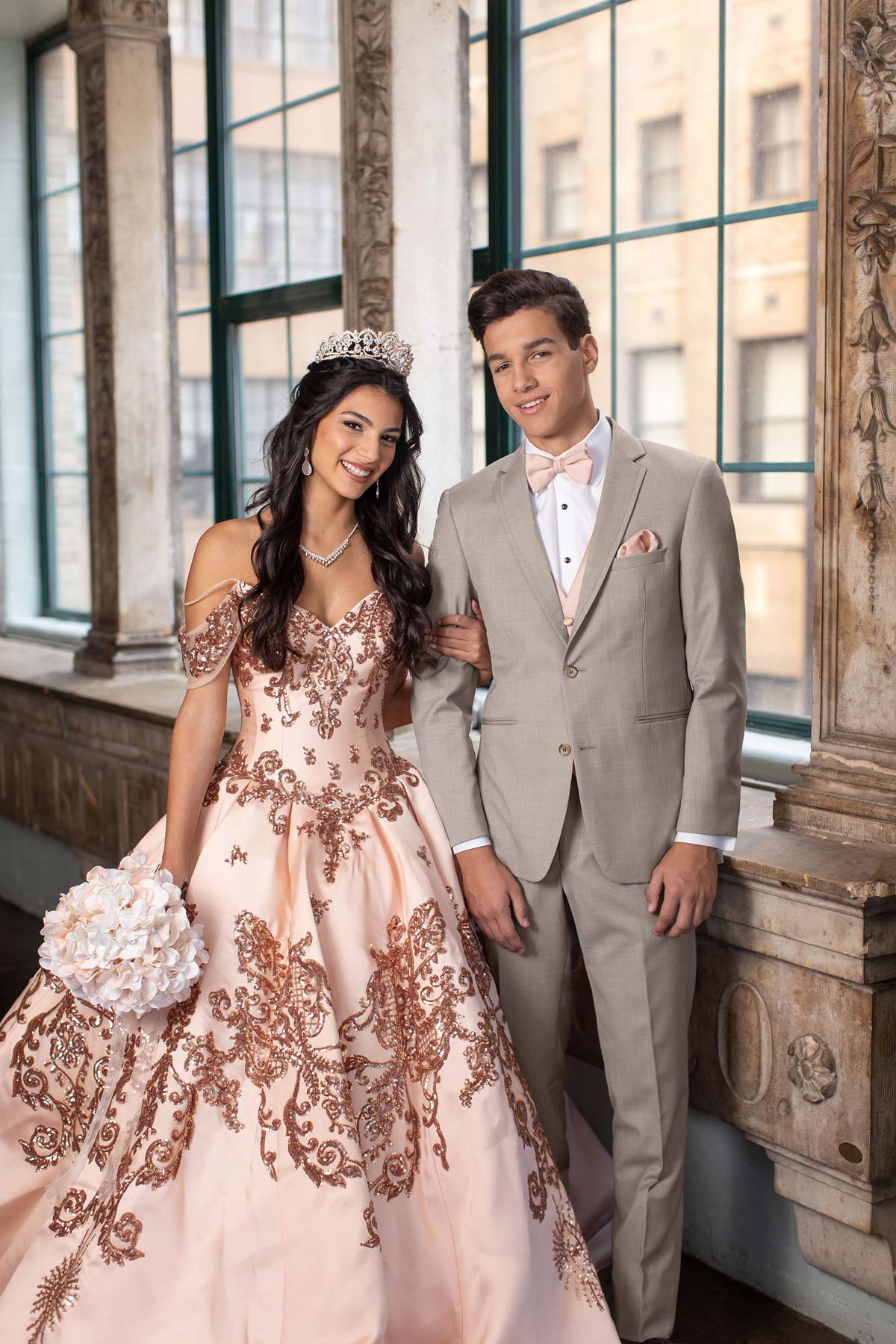 young hipanic man wearing a sand suit with pink bowtie and young hispanic lady wearing a pink gown