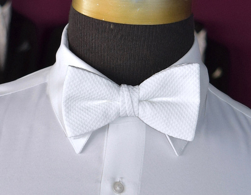 White pique bow tie on a mannequin wearing a white shirt against a dark background