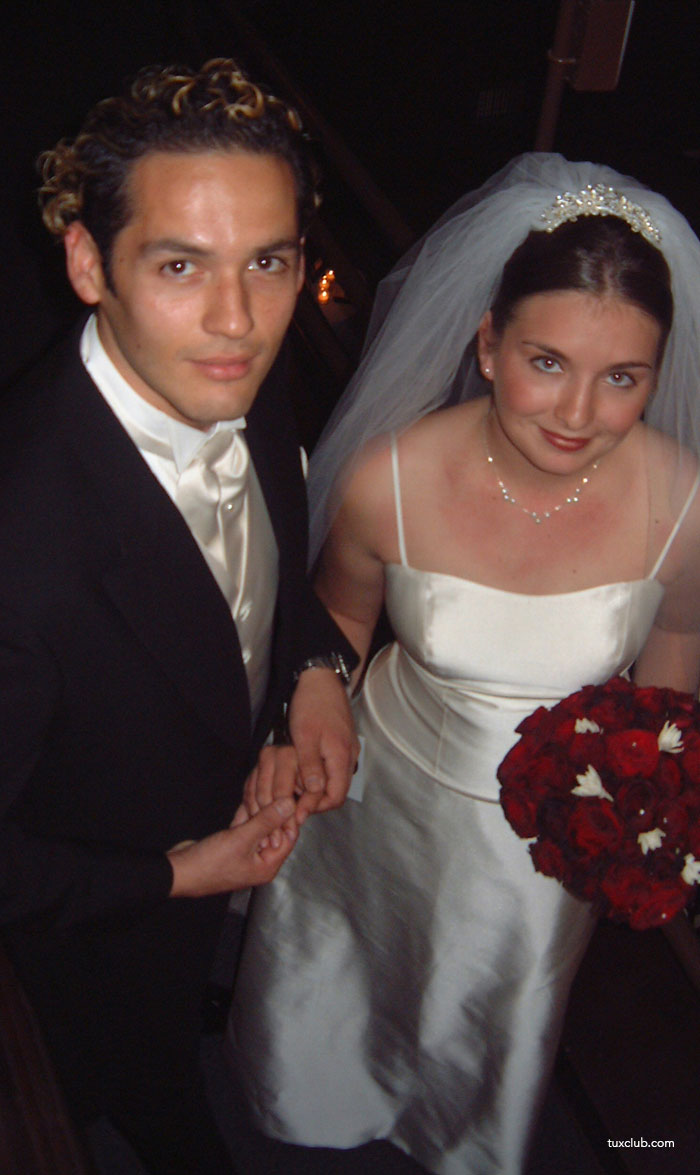 Man and woman on a wedding day, holding hands, with the man waring a black morning suit with ivory ascot and vest.