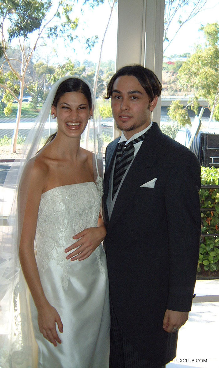 Groom wearing a charcoal cutaway morning suit with striped ascot and gray vest with a bride in an ivory wedding gown at a reception