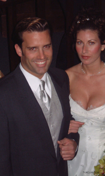 groom wearing a charcoal cutaway orning suit with gray vest and tie standing with a bride in white gown at a reception
