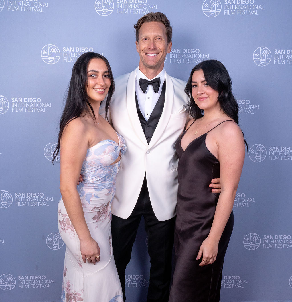 Handsome man wearing an ivory shawl collar tuxedo standing with 2 beautiful ladies.