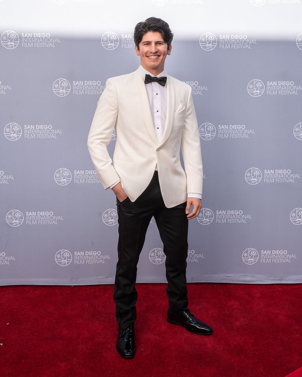 Actor wearing an off-white shawl collar tuxedo rental standing on the red carpet at the San Diego International Film Festival.