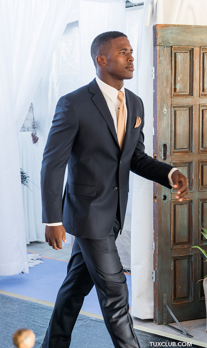 Man in a navy slim ft suit walking through a doorway with a blurred background