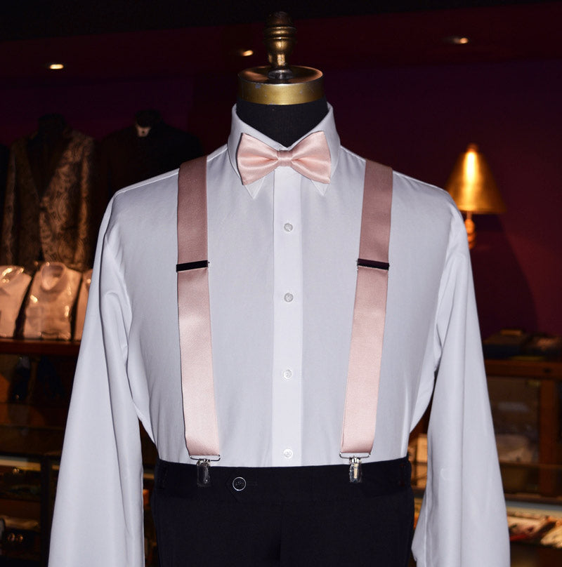 Mannequin wearing a white dress shirt with blush satin suspenders and a blush bow tie inside a tuxedo shop.