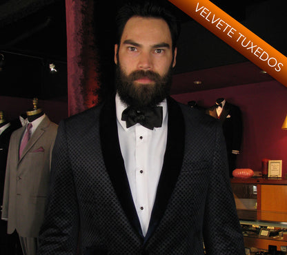 Man wearing a black velvet shawl collar tuxedo with a bow tie in a clothing store setting.