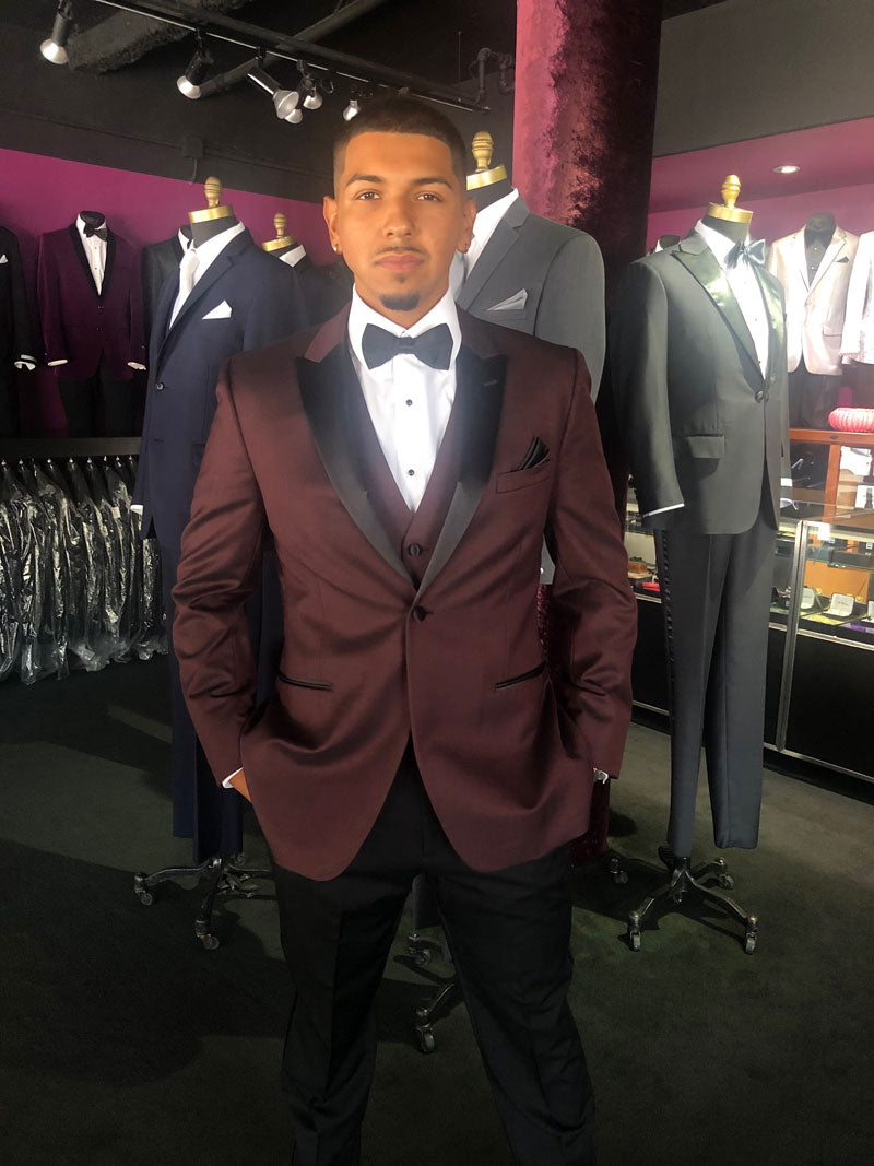 Man wearing a burgundy tuxedo in a formal wear store.