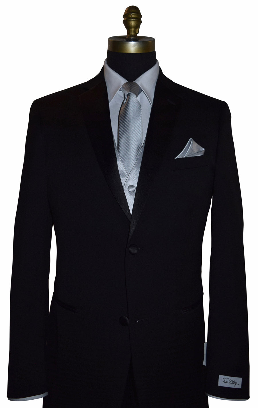 Black wedding suit with a "Tux Bling" branded label on the sleeve on a mannequin with a white shirt, silver necktie and silver vest, and pocket square.