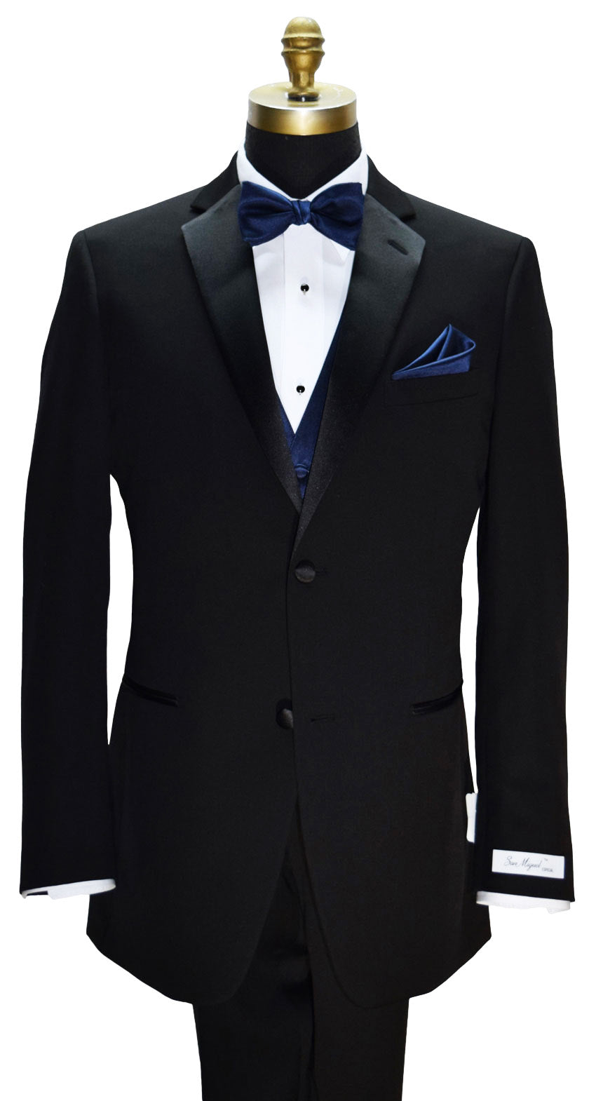 Black "San Miguel Especial" branded notch-lapel tuxedo with a marine-blue pre-tied bow tie and marine-blue tuxedo vest and pocket square on a mannequin against a white background