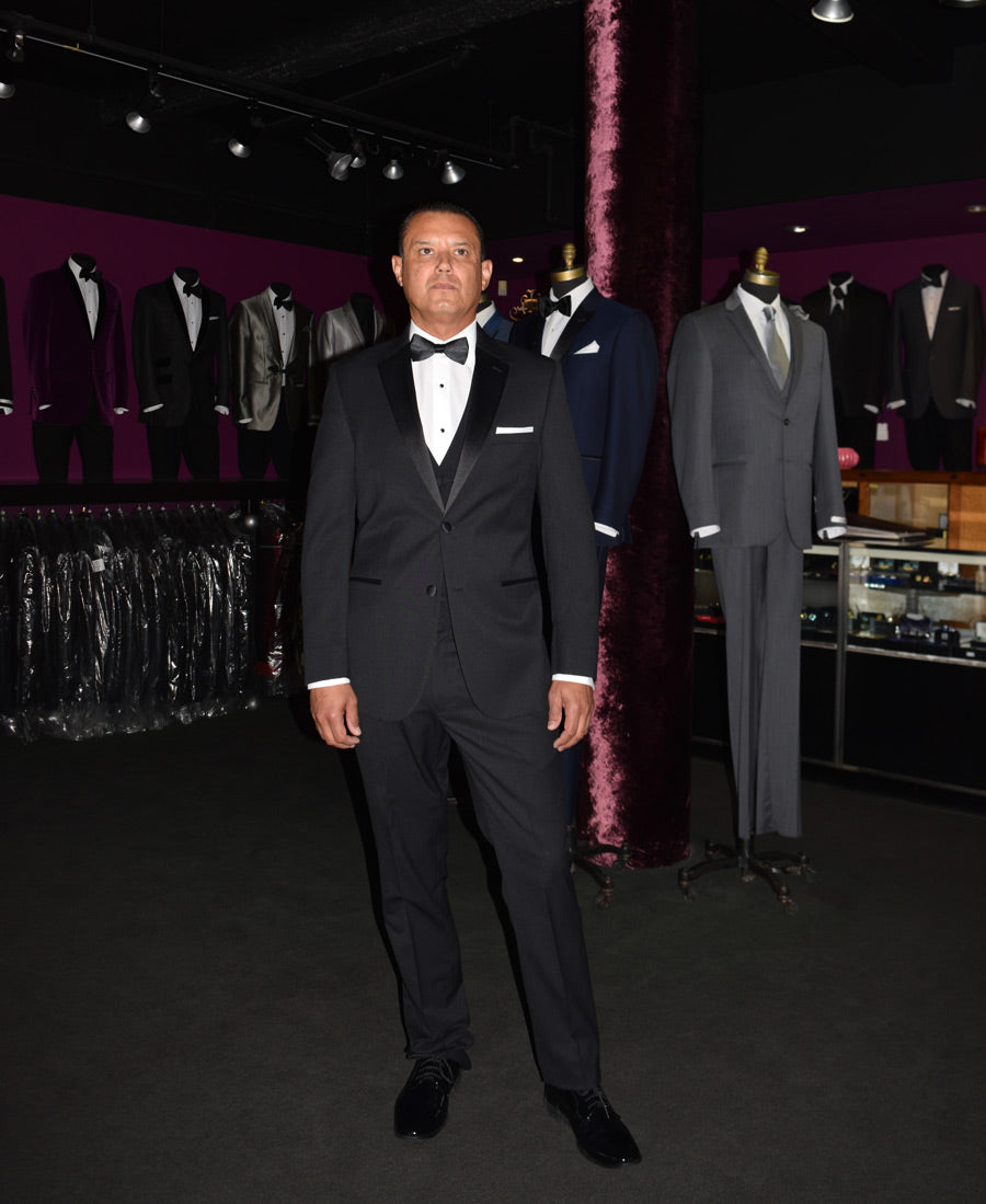 Groomsman wearing black two button notch tuxedo with a black vest and bowtie