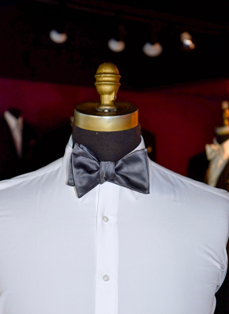 Mannequin wearing a white dress shirt with a charcoal "self-tie"  bow tie against a dark background