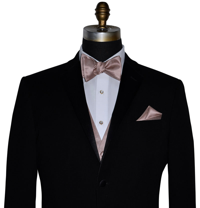 close-up black notch-lapel tuxedo with a white dress shirt and a rose-gold tuxedo vest and rose-gold "tie-yourself" bowtie and pocket handkerchief against a white background
