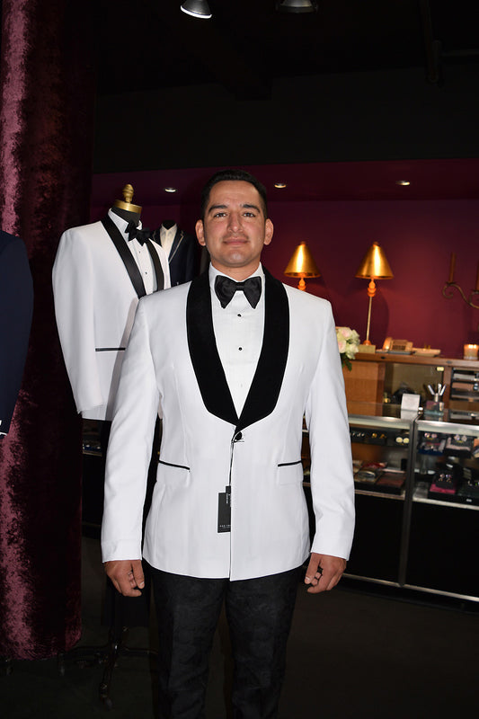 Man in a white tuxedo with black velvet shawl collar standing in a tuxedo shop 