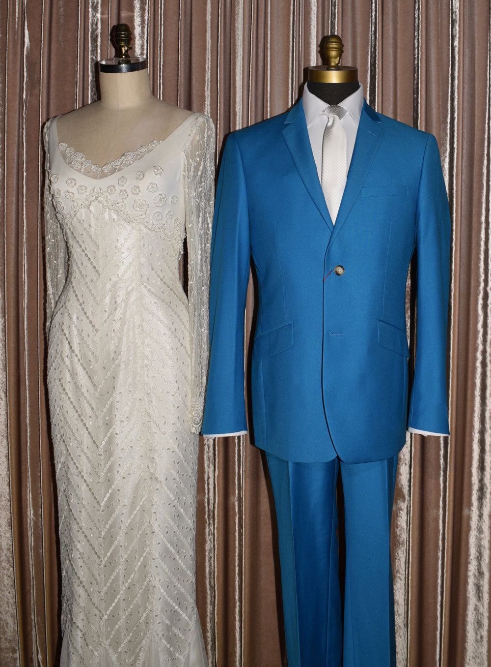 White wedding dress on a mannequin and electric blue suit on a mannequin against a curtain background