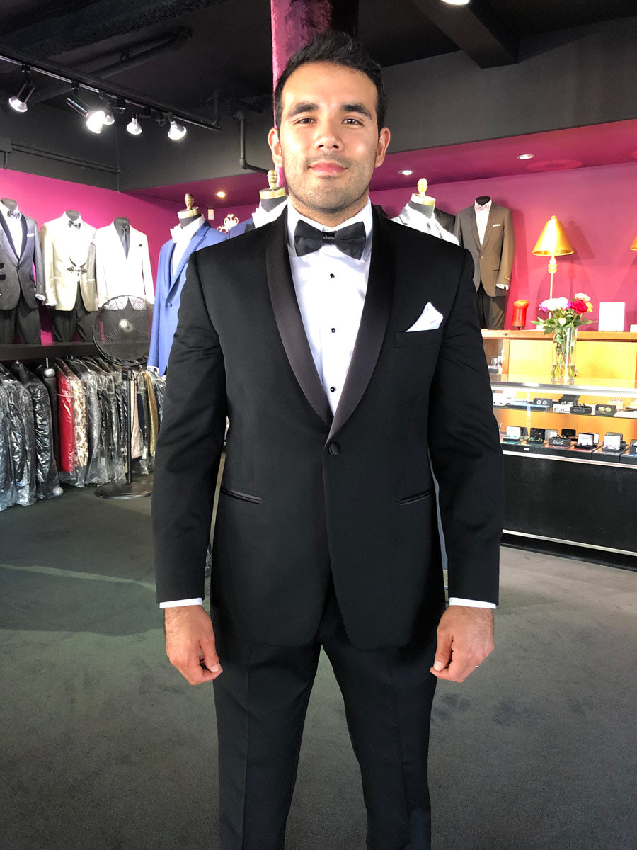 hispanic groom trying-on a black shawl collar tuxedo with a white plain front tuxedo shirt and black bowtie at a tuxedo shop