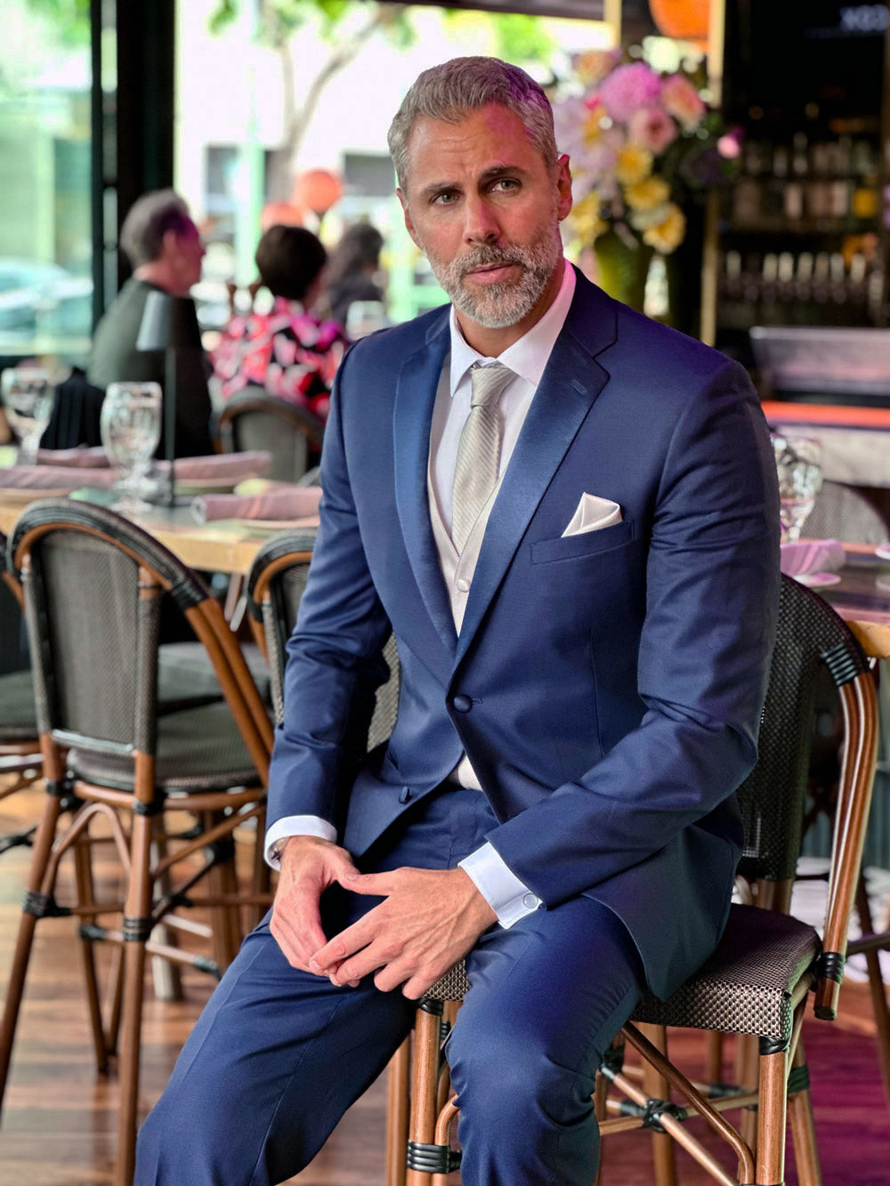 Handsome man wearing a navy blue notch-lapel tuxedo with blue lapel while sitting in a restaurant. 