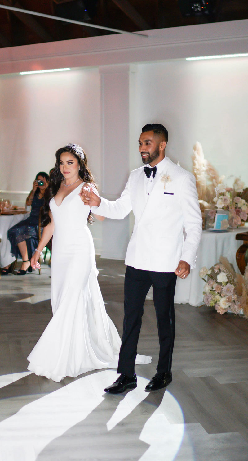 groom wearing off-white double breasted tuxedo jacket on a mannequin with a black bow tie walking with his bride against a white background