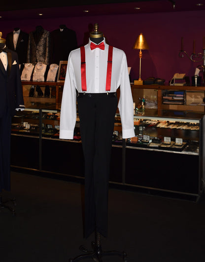 full length mannequin wearing a white shirt with a red bow tie and red satin suspenders in a store setting.