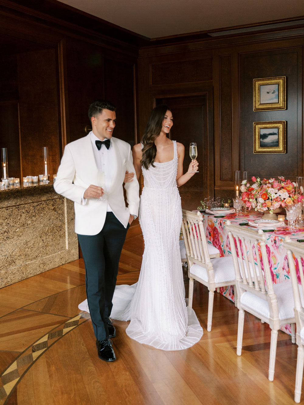 Groom wearing an ivory shawl collar tuxedo with black bowtie, and a bride wearing an off-white bridal gown, at bridal reception
