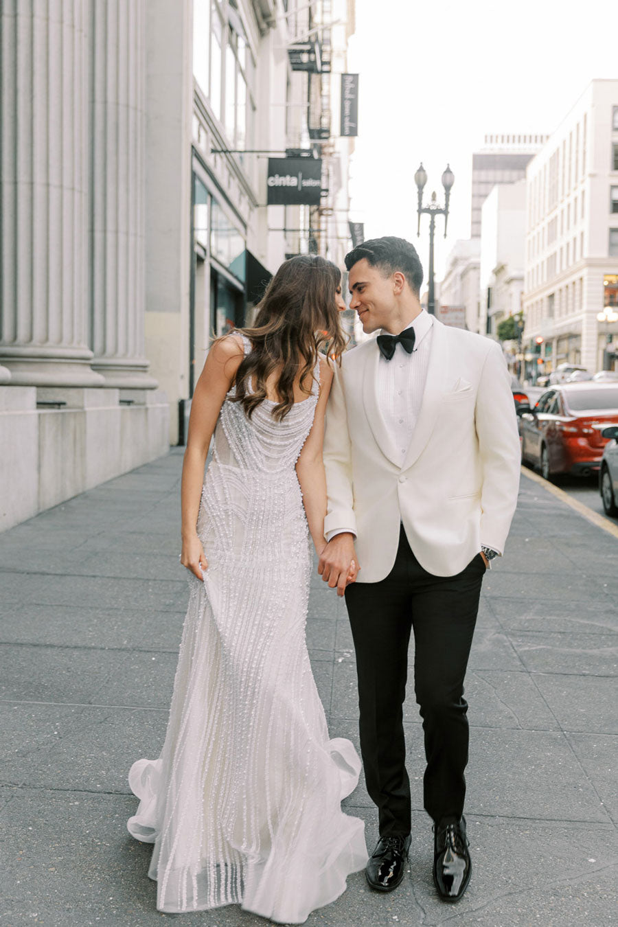 Groom wearing an ivory shawl collar tuxedo from  tuxclub in busy downtown with his bride in an ivory wedding gown
