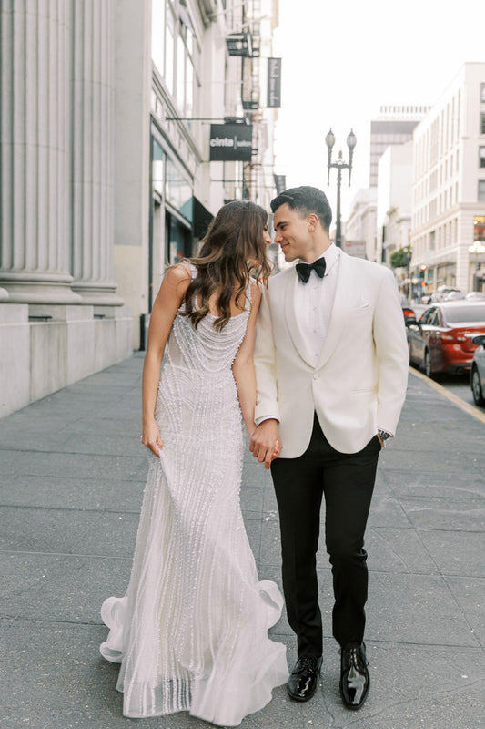 Groom wearing an ivory shawl collar tuxedo from  tuxclub in busy downtown with his bride in an ivory wedding gown