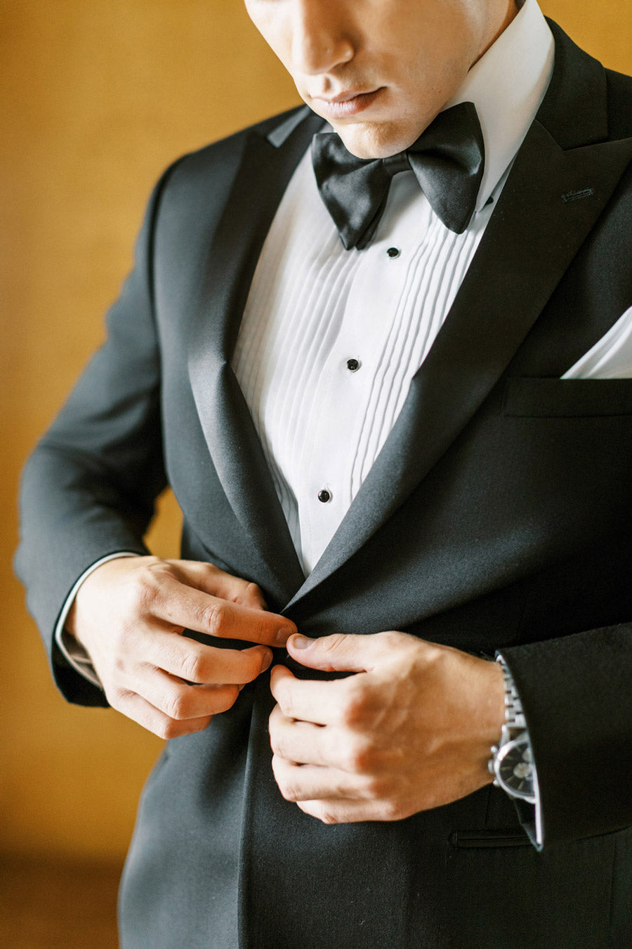 close up groom wearing black peak lapel tuxedo  with black satin bowtie and pleated shirt