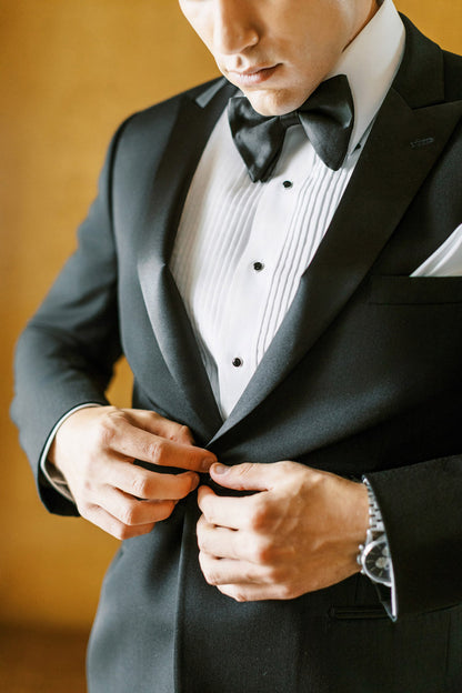 close up groom wearing black peak lapel tuxedo  with black satin bowtie and pleated shirt