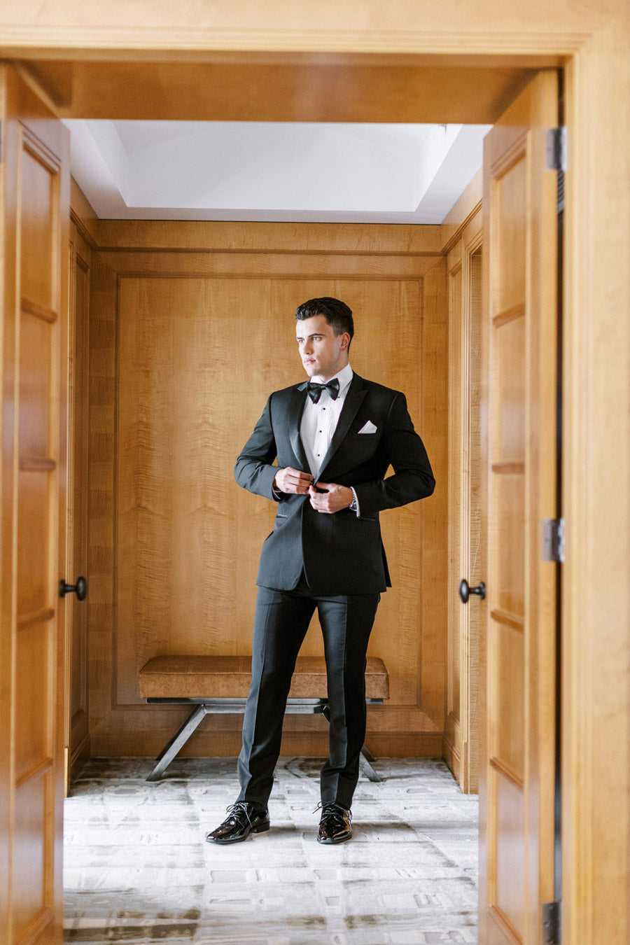 Groom wearing a Black peak lapel tuxedo with white pleated tuxedo shirt and black satin bowtie.