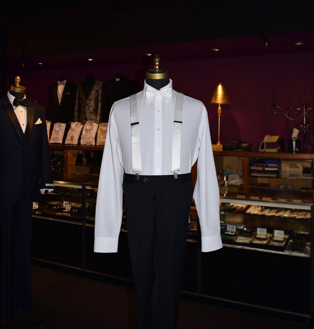 Mannequin wearing a white dress shirt with white satin suspenders and black pants in a store setting.