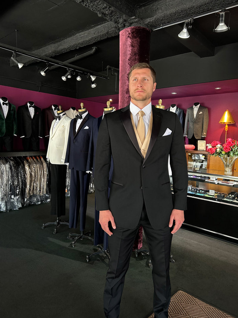 man wearing a black notch lapel tuxedo with a gold vest and gold long tie in a tuxedo shop