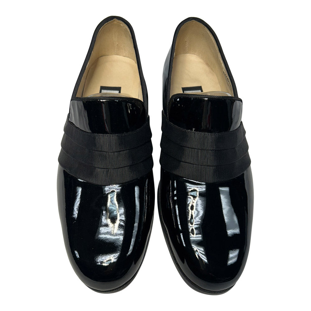 close-up view Pair of black patent leather slip-on shoes with a grosgrain ribbon detail on a white background