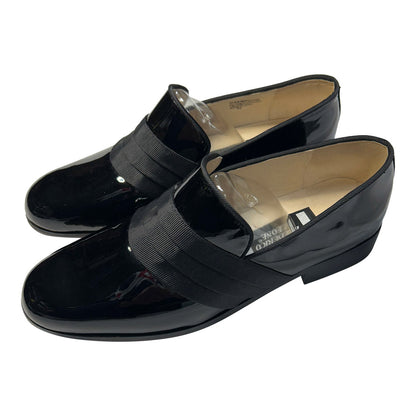 Pair of black patent leather slip-on shoes with a grosgrain ribbon detail on a white background