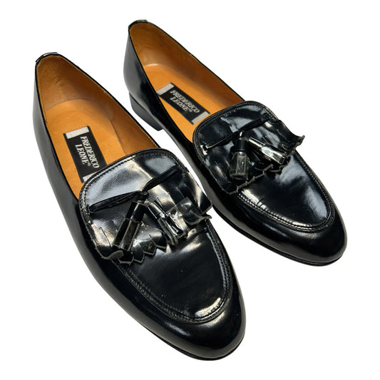 Pair of black patent leather slip-on loafers with tassels on a white background