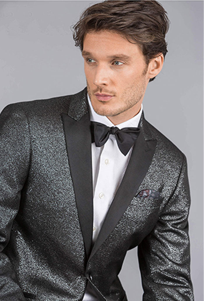 Man wearing a back tuxedo with shimmer and black peak lapels and black satin bow tie on a gray background