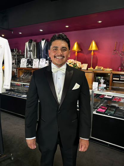 groom wearing a black peak lapel tuxedo with off-white bowtie and vest inside a tuxedo shop