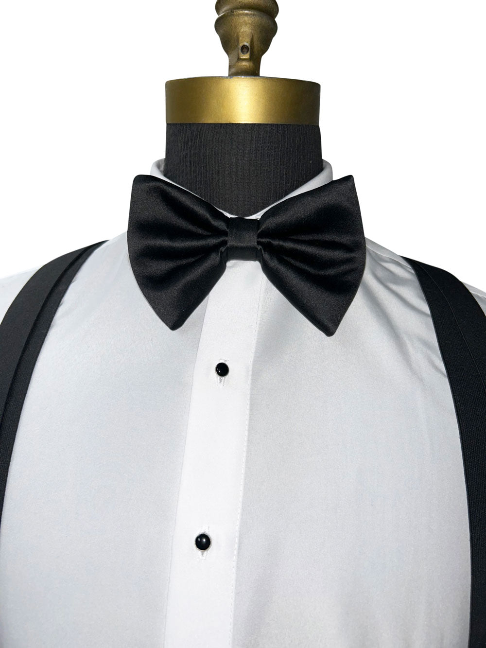Big black bow tie on a white shirt with black suspenders on a mannequin.