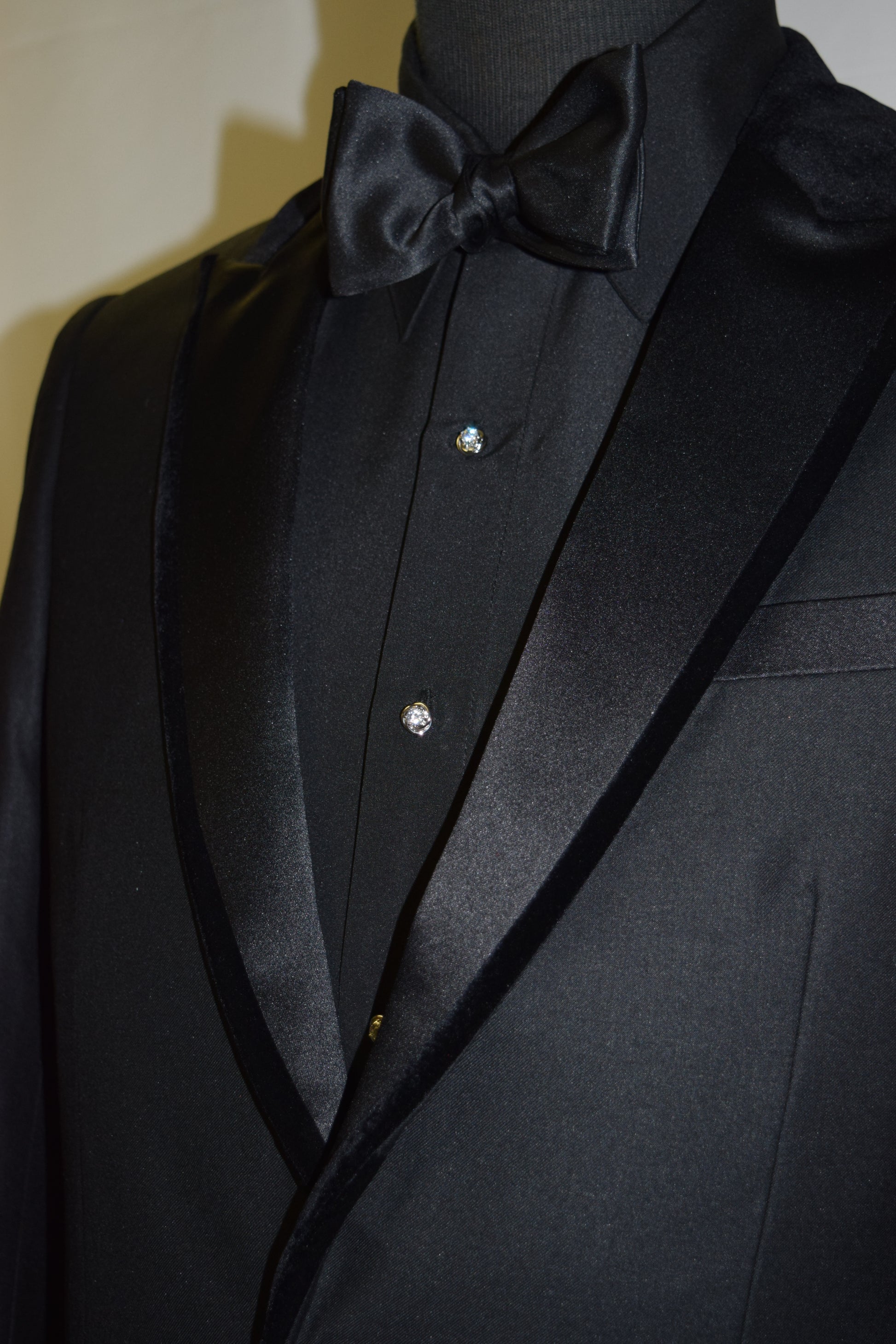 very close-up side view black peak lapel tuxedo with velvet on the edges of the lapel wearing a black tuxedo shirt with a black bowtie