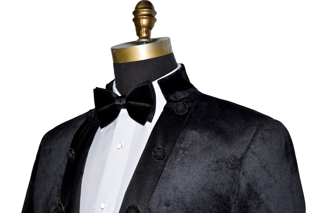 side view black velvet nehru collar tuxedo jacket with a black bowtie against a white background
